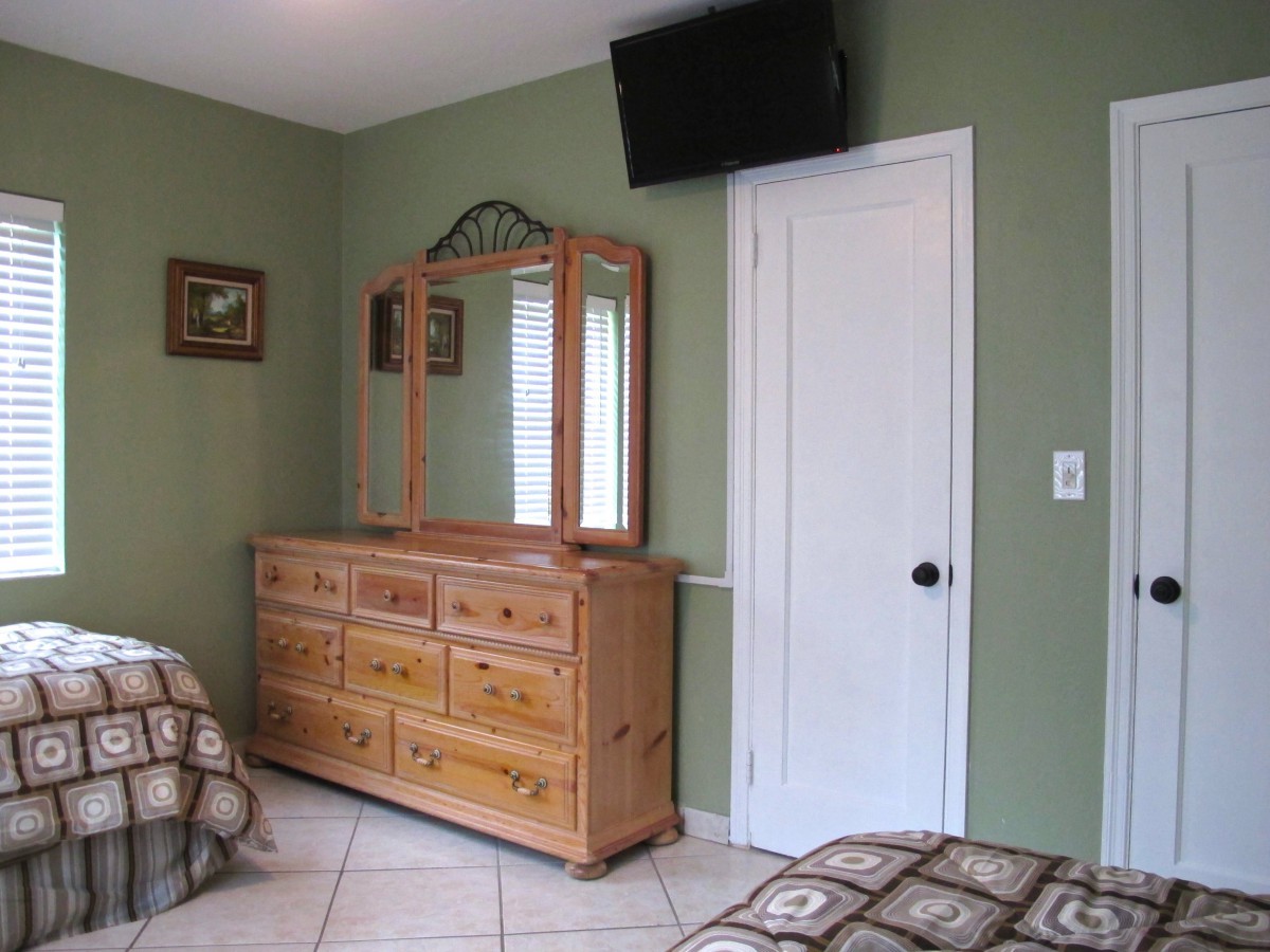 A bedroom with a wooden dresser and mirror, a wall-mounted TV, and green walls.