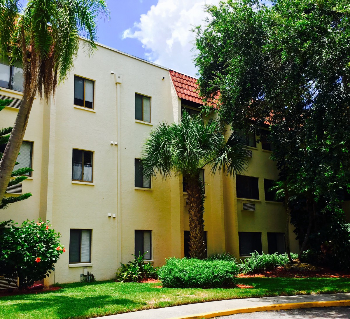A sunny day view of an apartment building surrounded by lush greenery and trees.