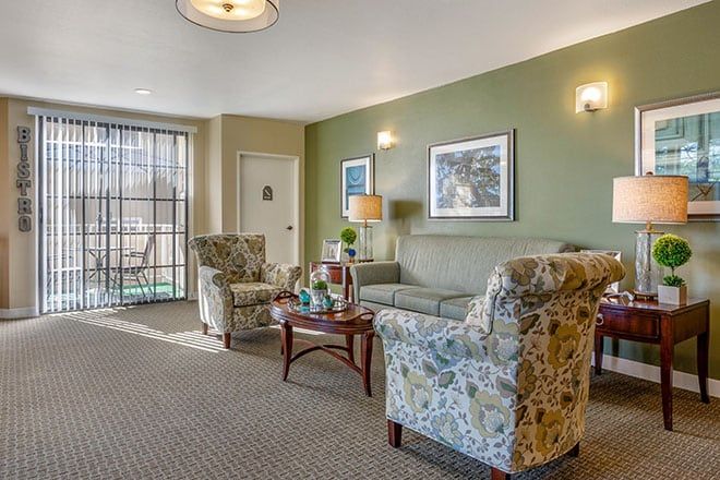 A cozy living room with floral-patterned chairs, a sofa, and a central table complemented by artwork and a lamp.