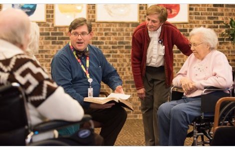 A group of people engaged in a discussion, with one person holding a book.