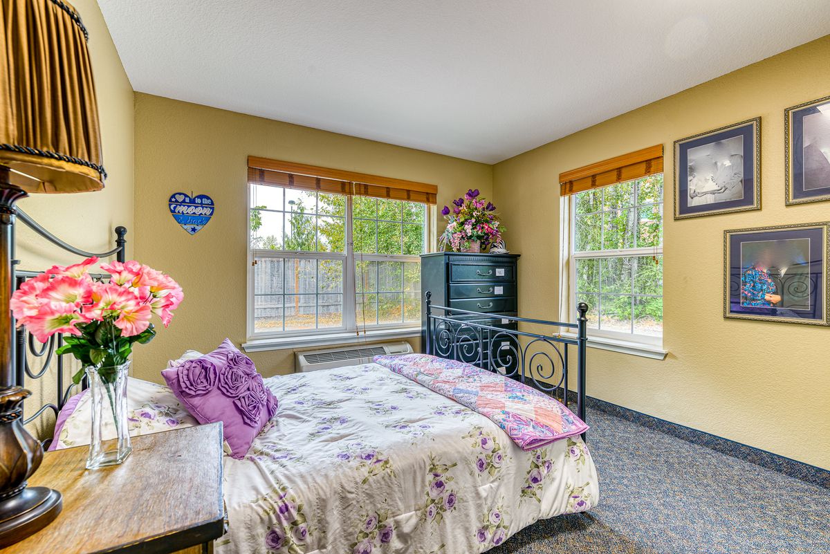 A cozy bedroom with floral bedding and ample natural light from large windows.