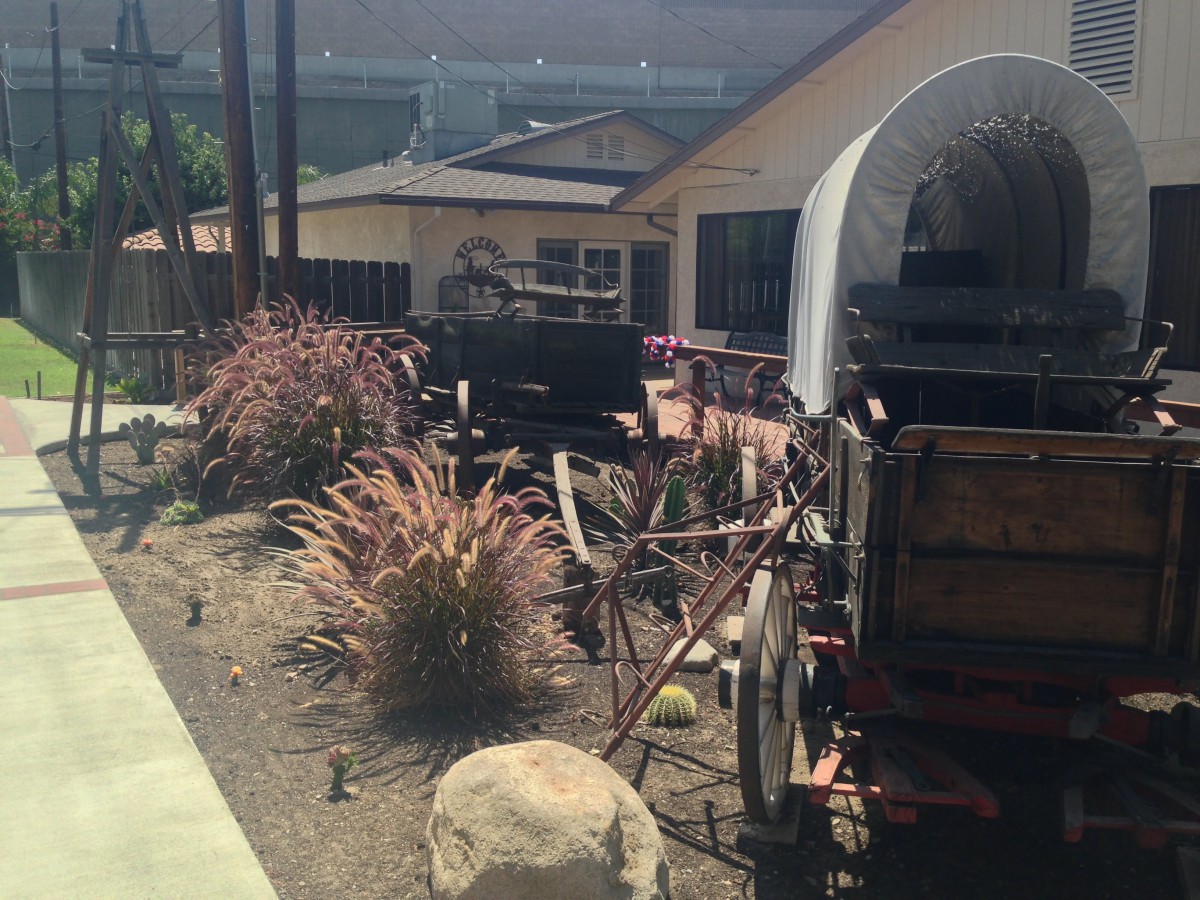 A historical covered wagon displayed outdoors near a ranch-style building with desert plants.