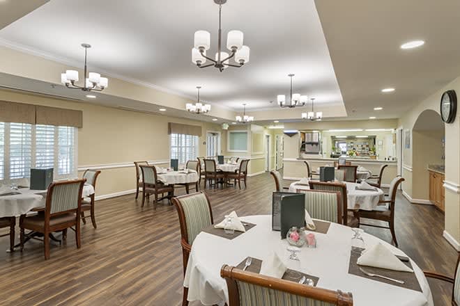An elegantly decorated dining area with neatly arranged tables and chairs, illuminated by chandeliers.