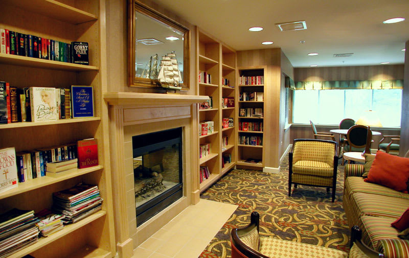 A cozy library with bookshelves, a fireplace, and comfortable seating.