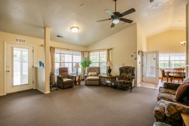 A cozy living room with armchairs, a ceiling fan, and large windows allowing natural light.