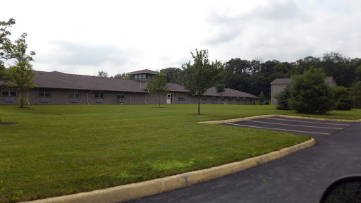 A view of a modern building surrounded by lush grass and trees under a cloudy sky.
