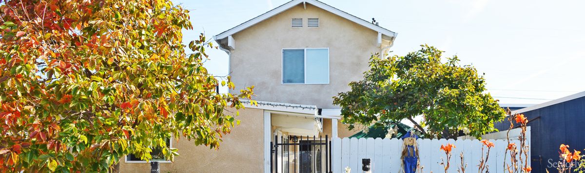 A two-story residential house with a gated entrance and surrounding trees.