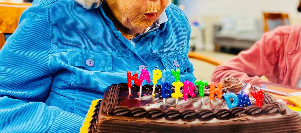 A person blowing out candles on a chocolate birthday cake.