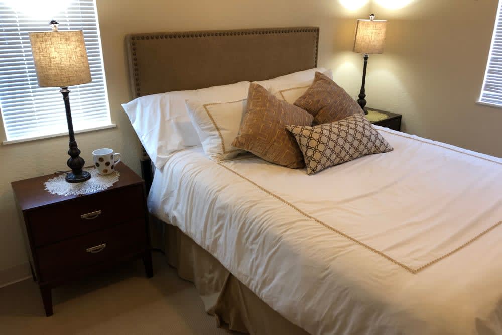 A cozy bedroom with a neatly made bed, adorned with multiple pillows and illuminated by a bedside lamp.