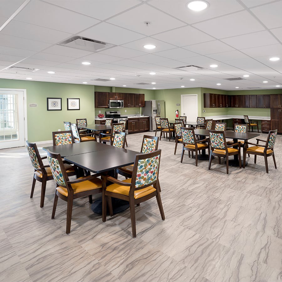 A modern dining area with multiple tables and chairs, adjacent to a kitchen in a community space.