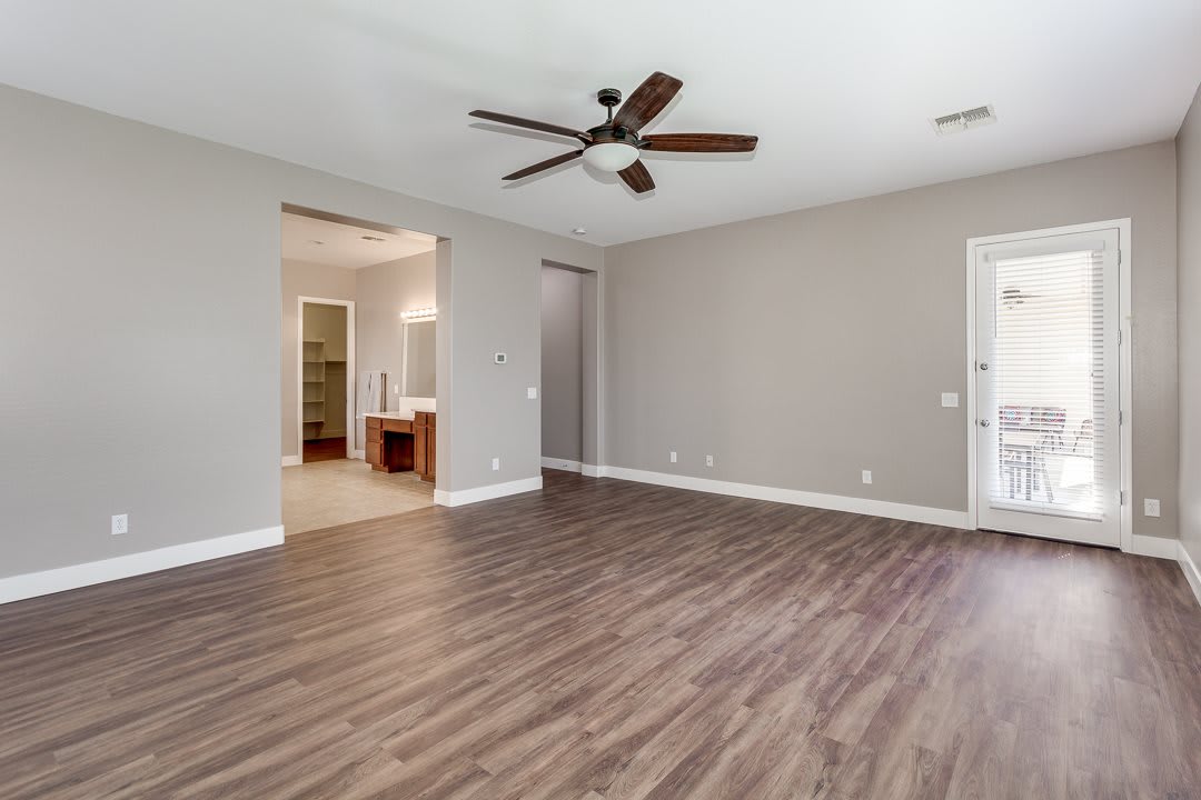 An empty room with hardwood flooring and a ceiling fan, featuring neutral-colored walls and an open doorway to another area.