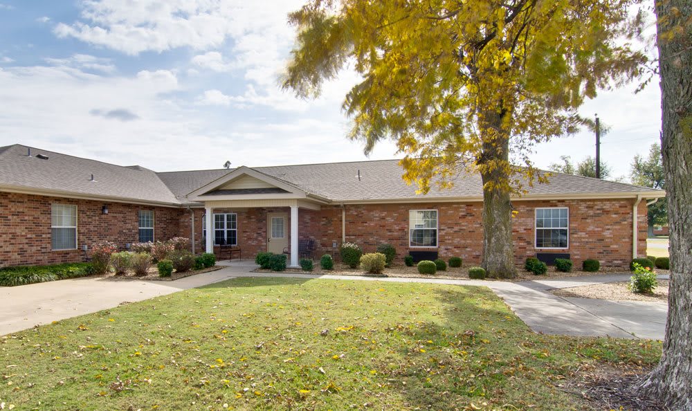 A brick residential house with a spacious lawn and a tree in the front yard.