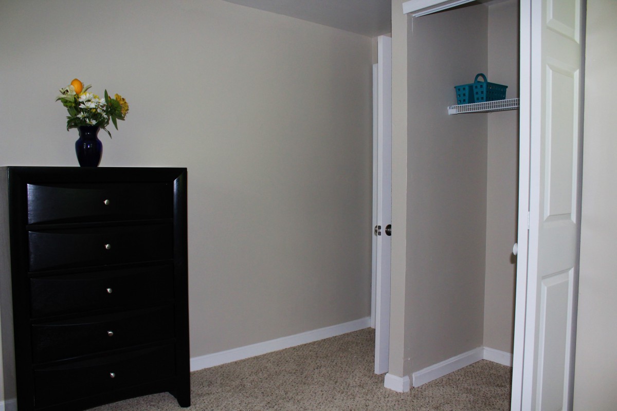 A minimalist bedroom featuring a dresser, an open closet, and neutral-colored walls.