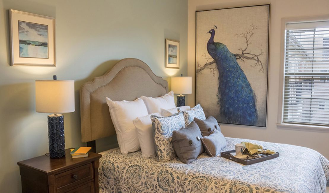 A cozy bedroom featuring a bed with patterned bedding and a large peacock painting above the headboard.