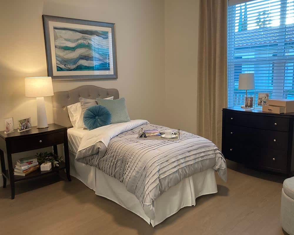 A cozy bedroom with a single bed, nightstand, and window, featuring a decorative painting above the headboard.
