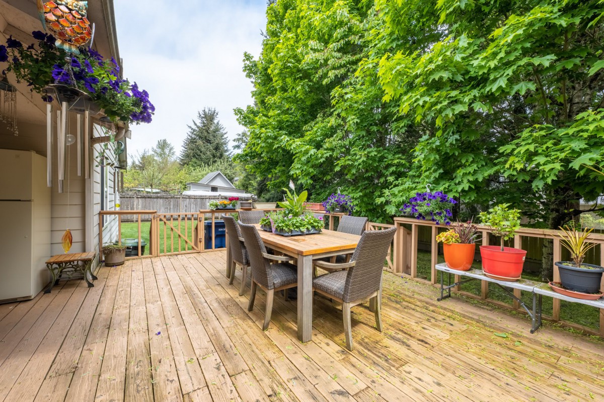 A wooden deck with outdoor furniture and colorful potted plants, surrounded by lush greenery.