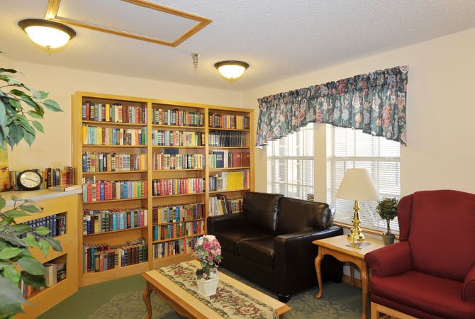 A cozy living room with a large bookshelf, brown sofa, and coffee table next to a window.
