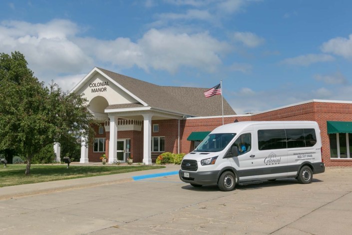 A van parked outside a brick building with a columned entrance under a cloudy sky.