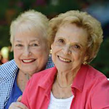 Two elderly women smiling and enjoying time together outdoors.
