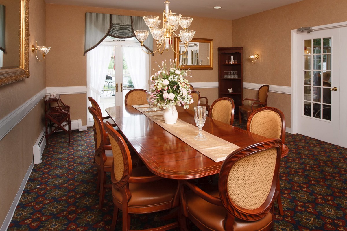 An elegant dining room with a long wooden table, upholstered chairs, and a decorative chandelier.