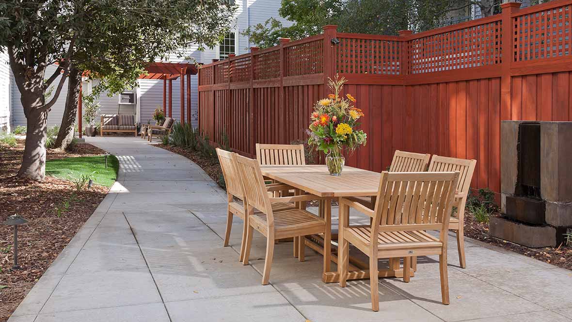 Wooden patio furniture set with a floral centerpiece in an outdoor garden setting.