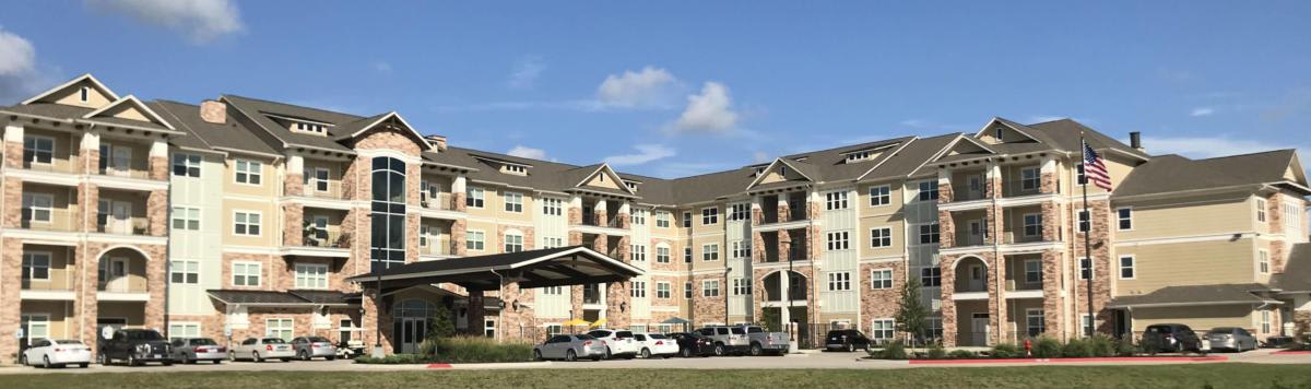 A suburban residential building with multiple floors, featuring parked cars in front.