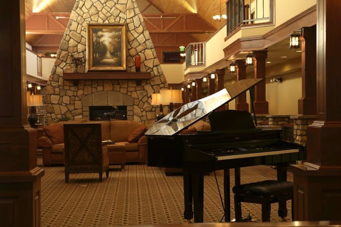 A cozy living room with a grand piano and a stone fireplace.