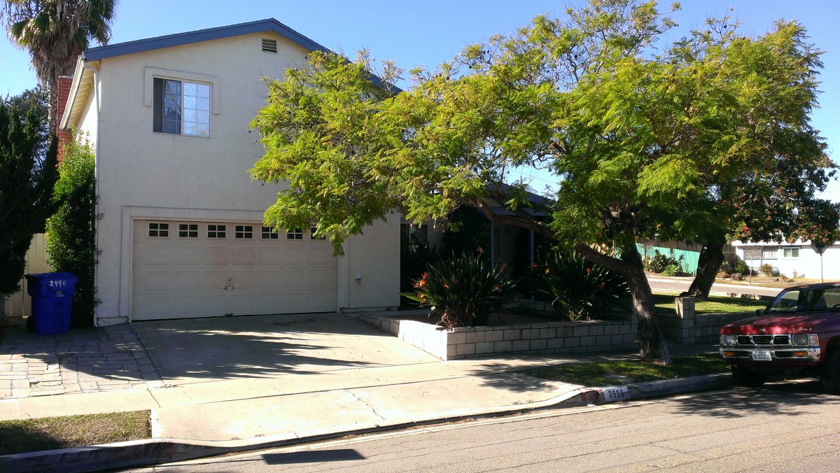 A suburban house with a garage and a large tree in the front yard.