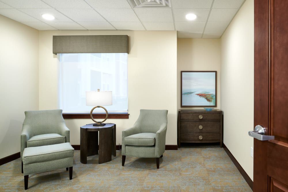 A well-lit waiting room with armchairs and a side table under a window.