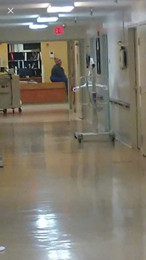 A hospital hallway with medical equipment and a distant view of a person near the reception area.