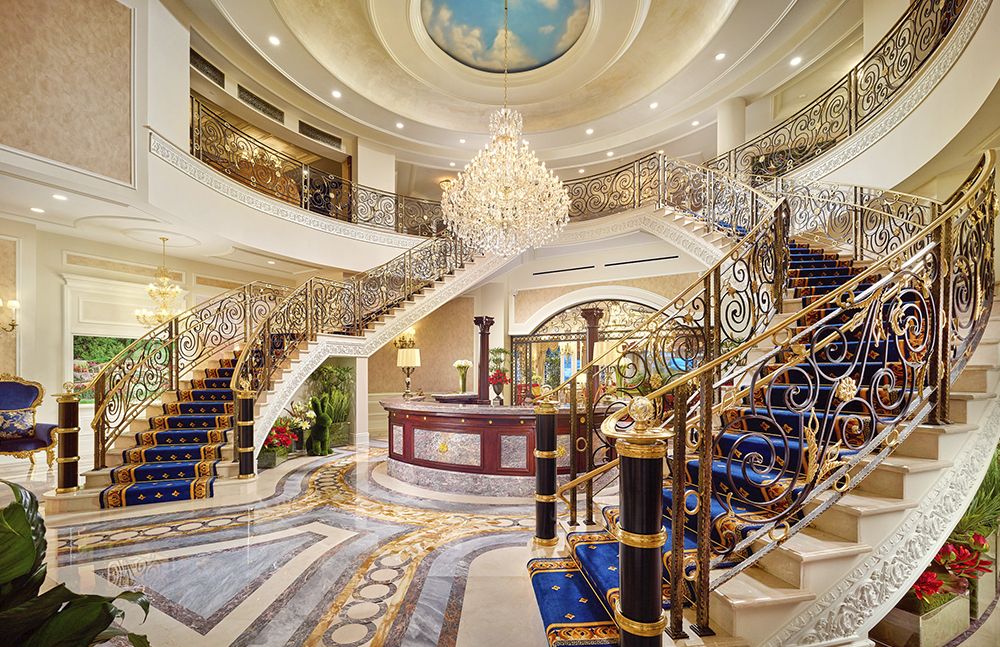 A luxurious hotel lobby with an ornate staircase and grand chandelier.