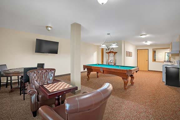A cozy game room featuring a pool table, seating area with a chess board, and a wall-mounted television.