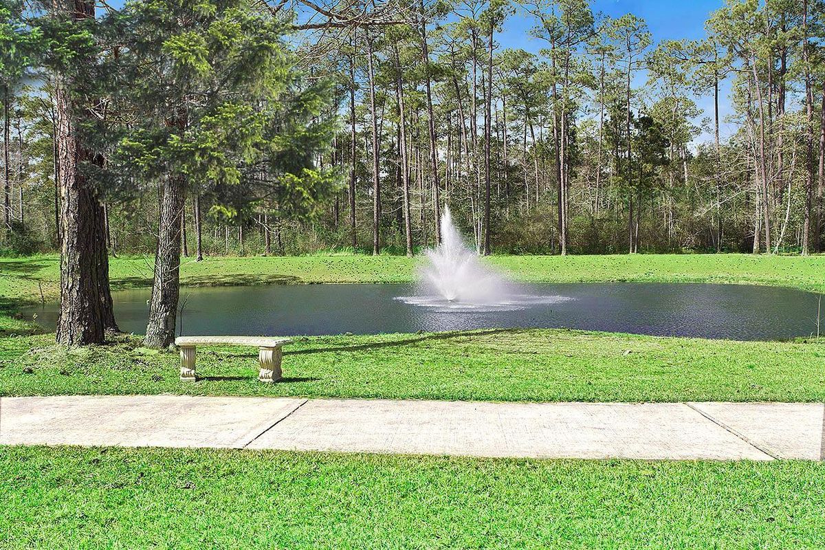 A serene park setting with a fountain in a pond, surrounded by trees and greenery.