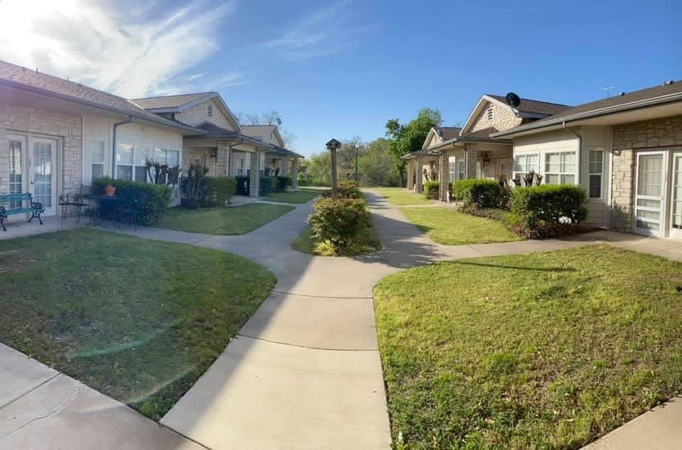 A serene residential area with a sunny pathway surrounded by houses and greenery.
