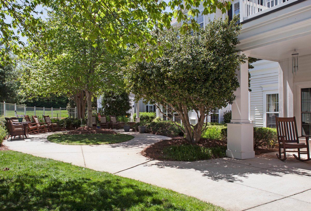 A tidy garden with trees and bushes lining a curved sidewalk in front of a house.