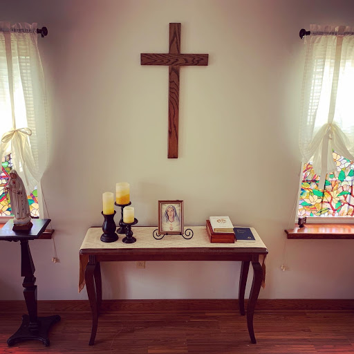 A serene interior space featuring a wooden cross on the wall, surrounded by decorative elements such as candles and a table with personal items.