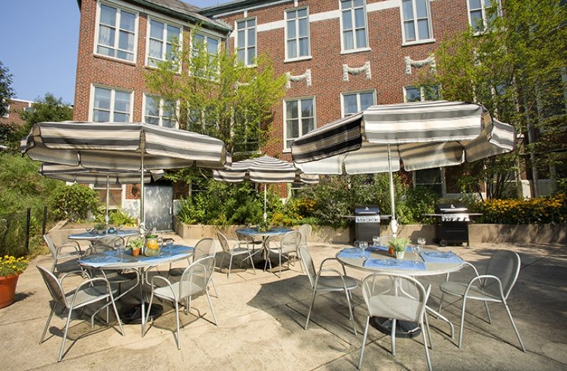 A cozy outdoor cafe patio with tables, chairs, and umbrellas surrounded by greenery.