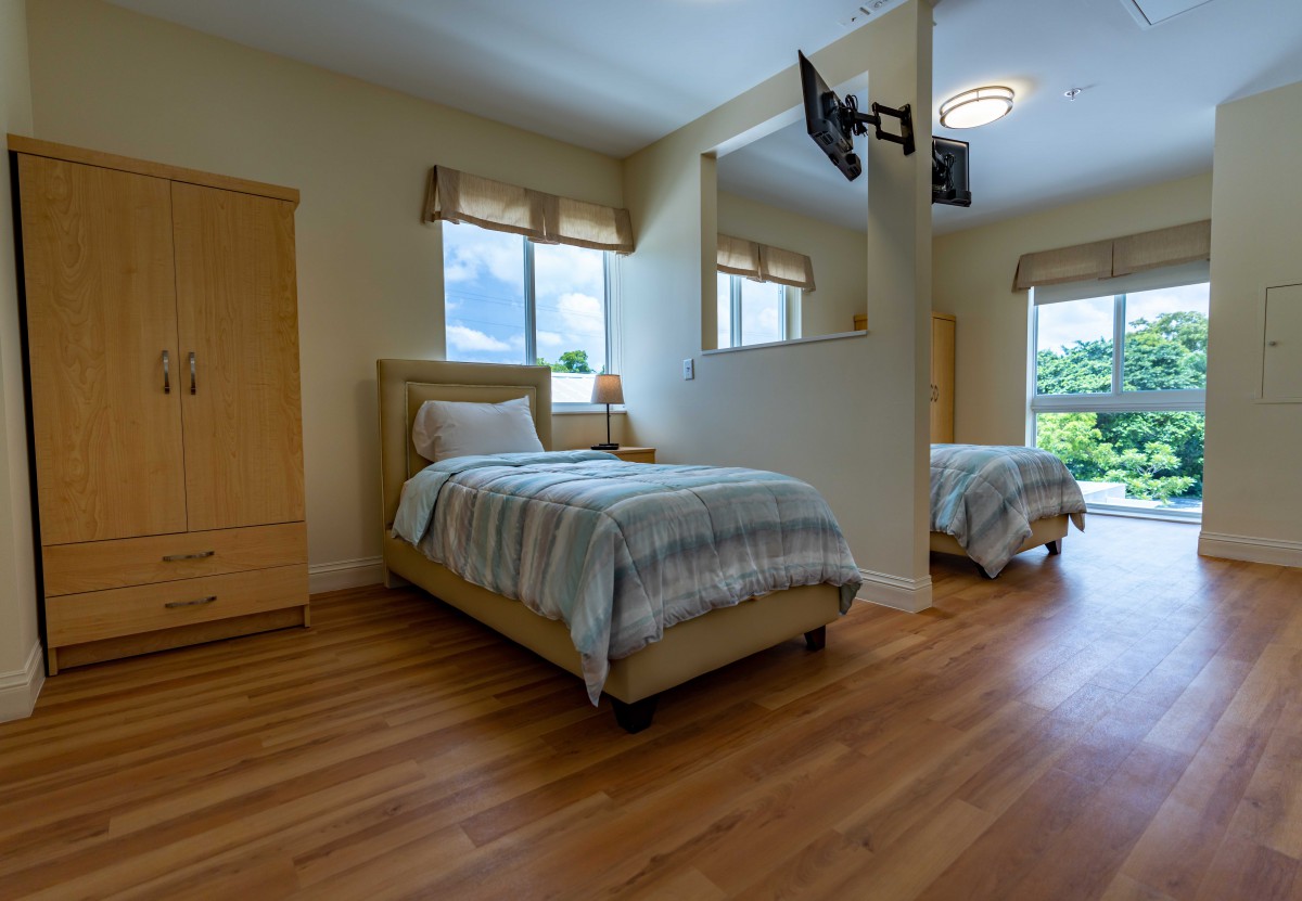 A cozy bedroom with two single beds, wooden flooring, and ample natural light through large windows.