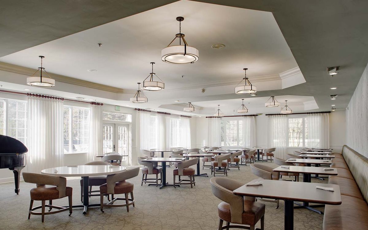 An empty dining area with neatly arranged tables and chairs under elegant lighting.