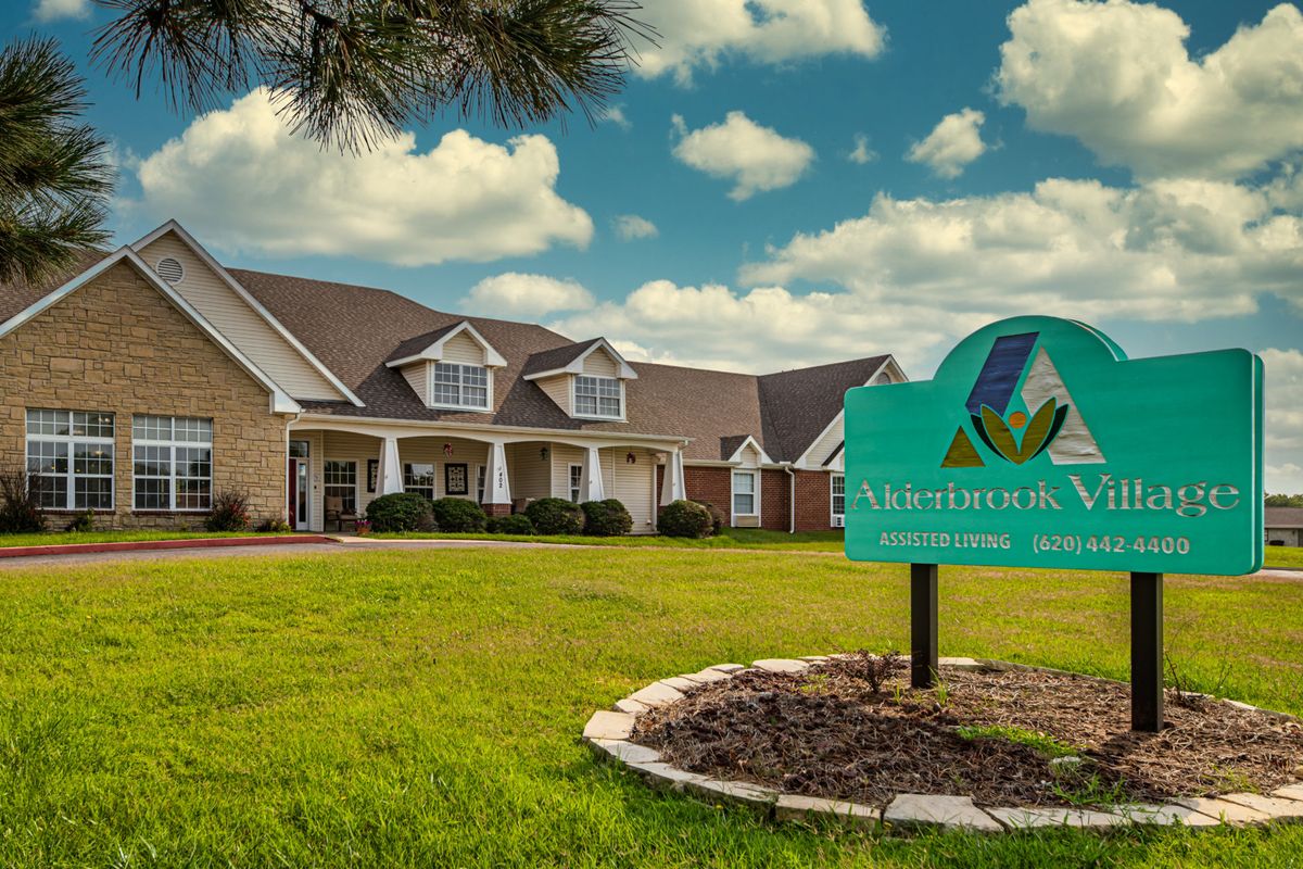 A suburban building with a manicured lawn and an informational sign under a partly cloudy sky.