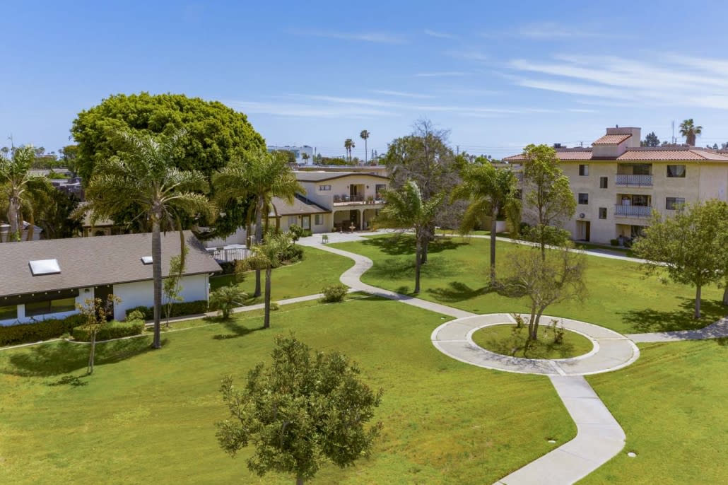 A scenic view of a landscaped garden with pathways, surrounded by buildings and lush greenery on a sunny day.