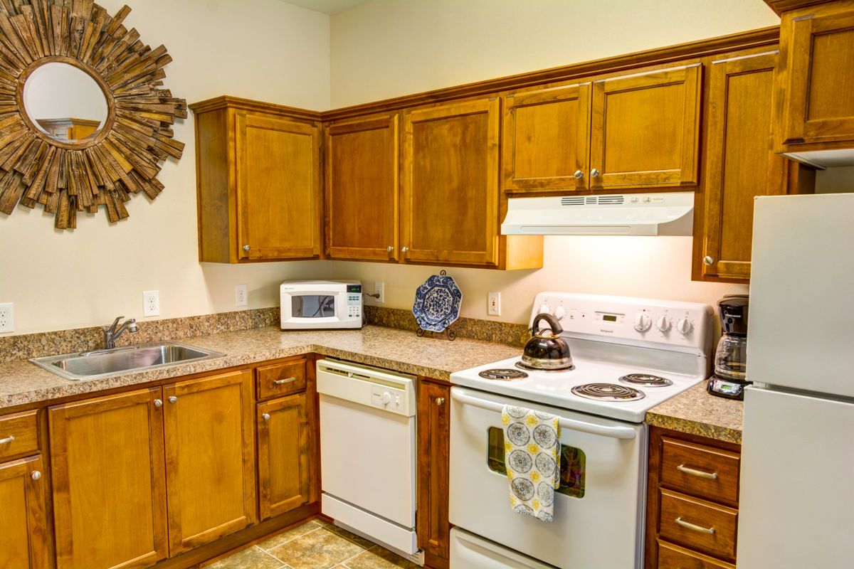 A cozy kitchen with wooden cabinets and various appliances, including a stove, oven, microwave, and dishwasher.