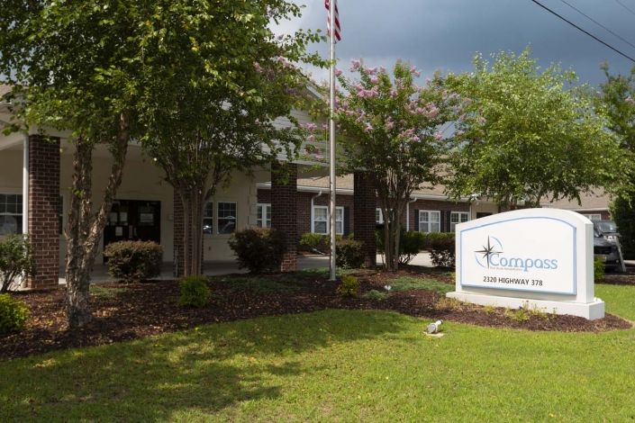 A school building with a sign in the foreground surrounded by trees and a flagpole.