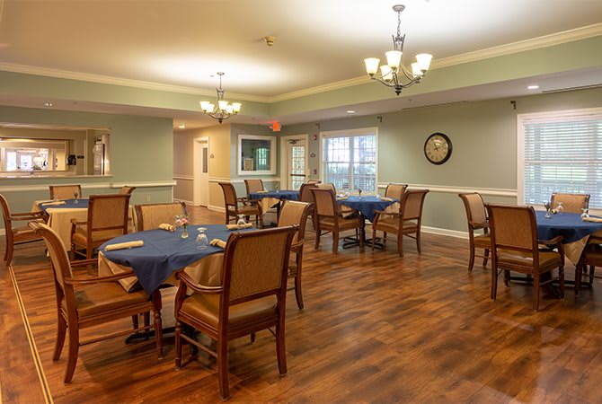 A cozy dining room with several tables and chairs arranged neatly, featuring warm lighting and wood flooring.