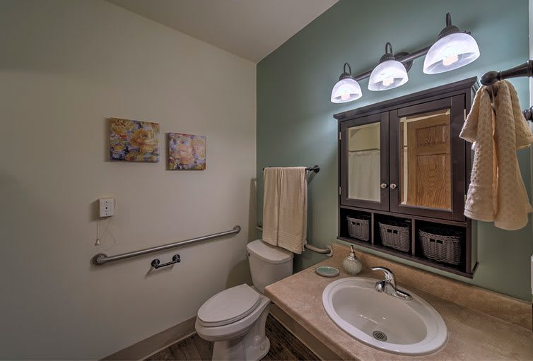 A clean and well-organized bathroom featuring a sink, mirror, and toilet with modern lighting and decor.