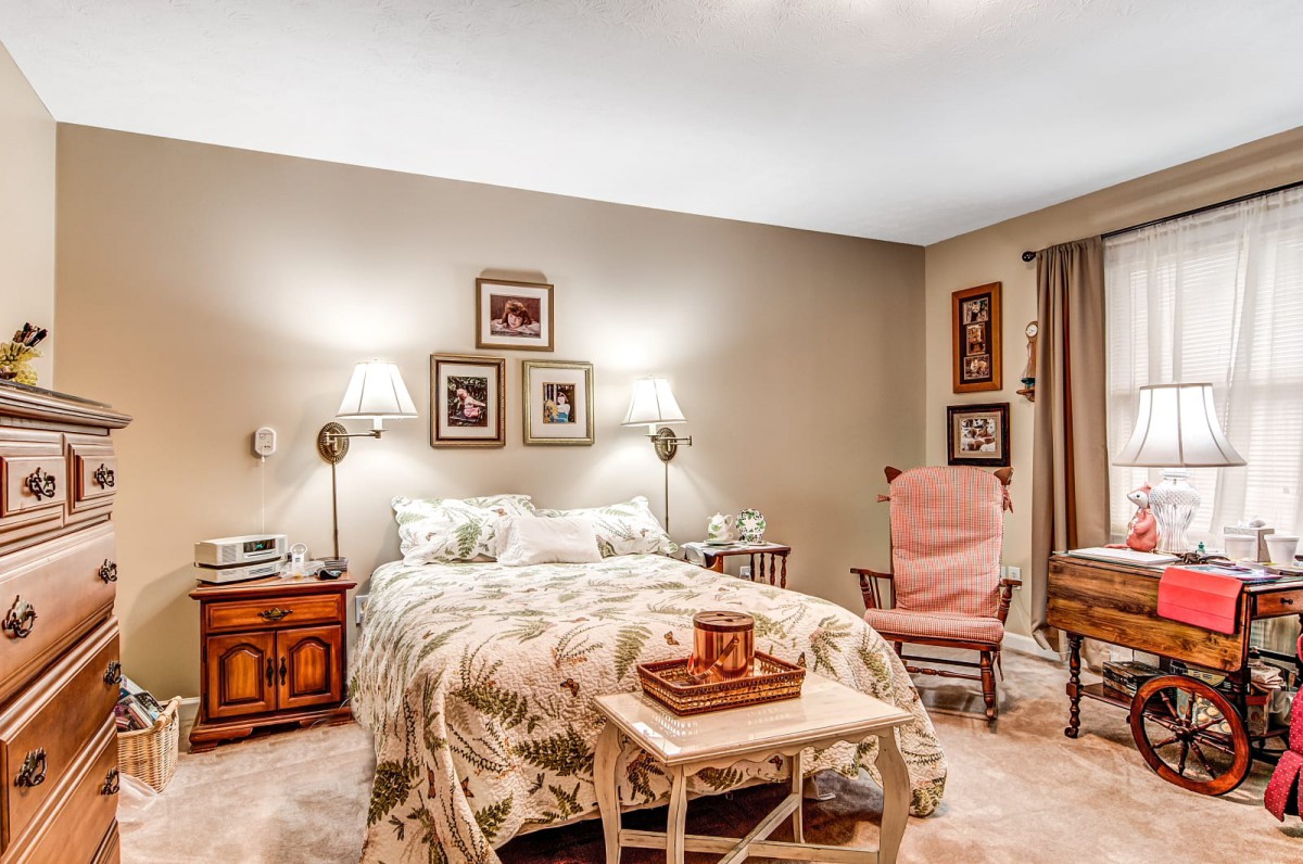 A cozy and traditionally decorated bedroom with a comfortable bed, wall lamps, and framed art.