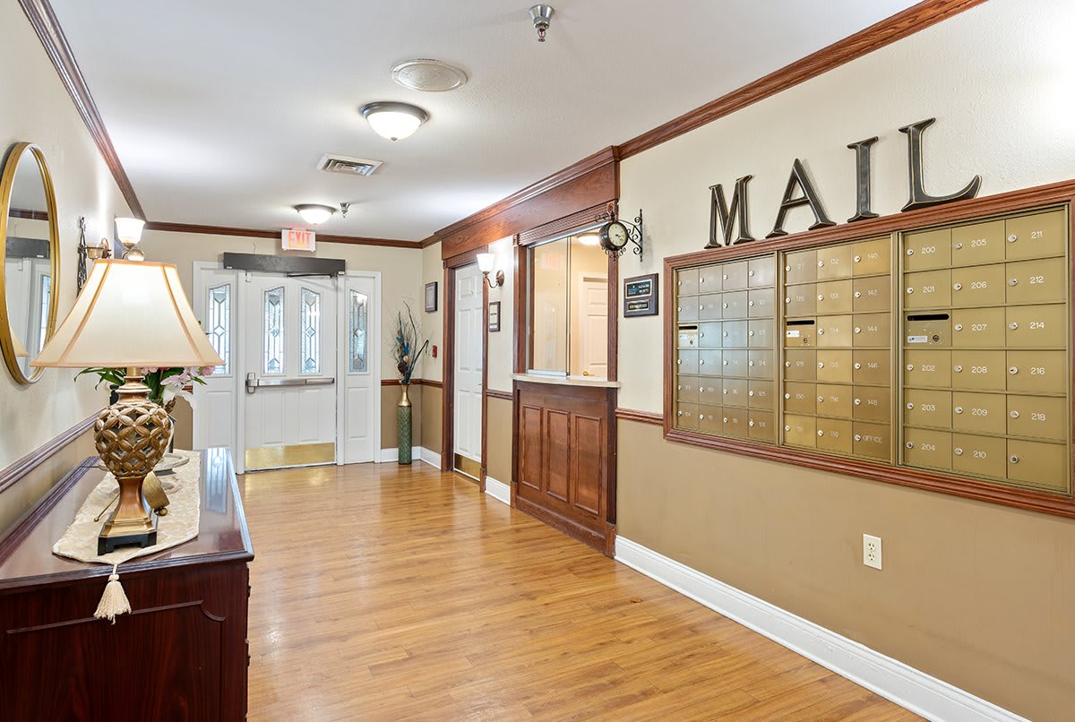 A well-lit hallway featuring a mailroom with wooden flooring and organized mailboxes.