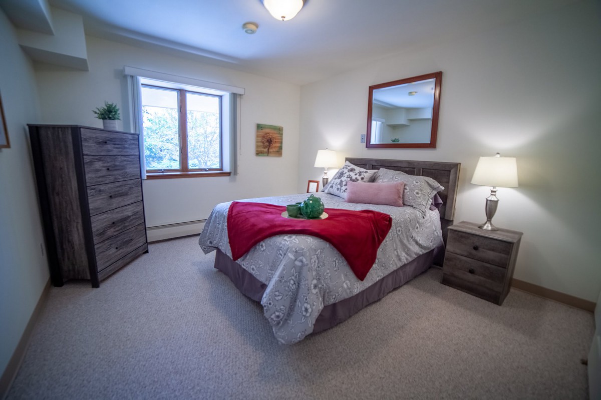 A cozy bedroom with a neatly made bed, bedside lamps, and a large window.