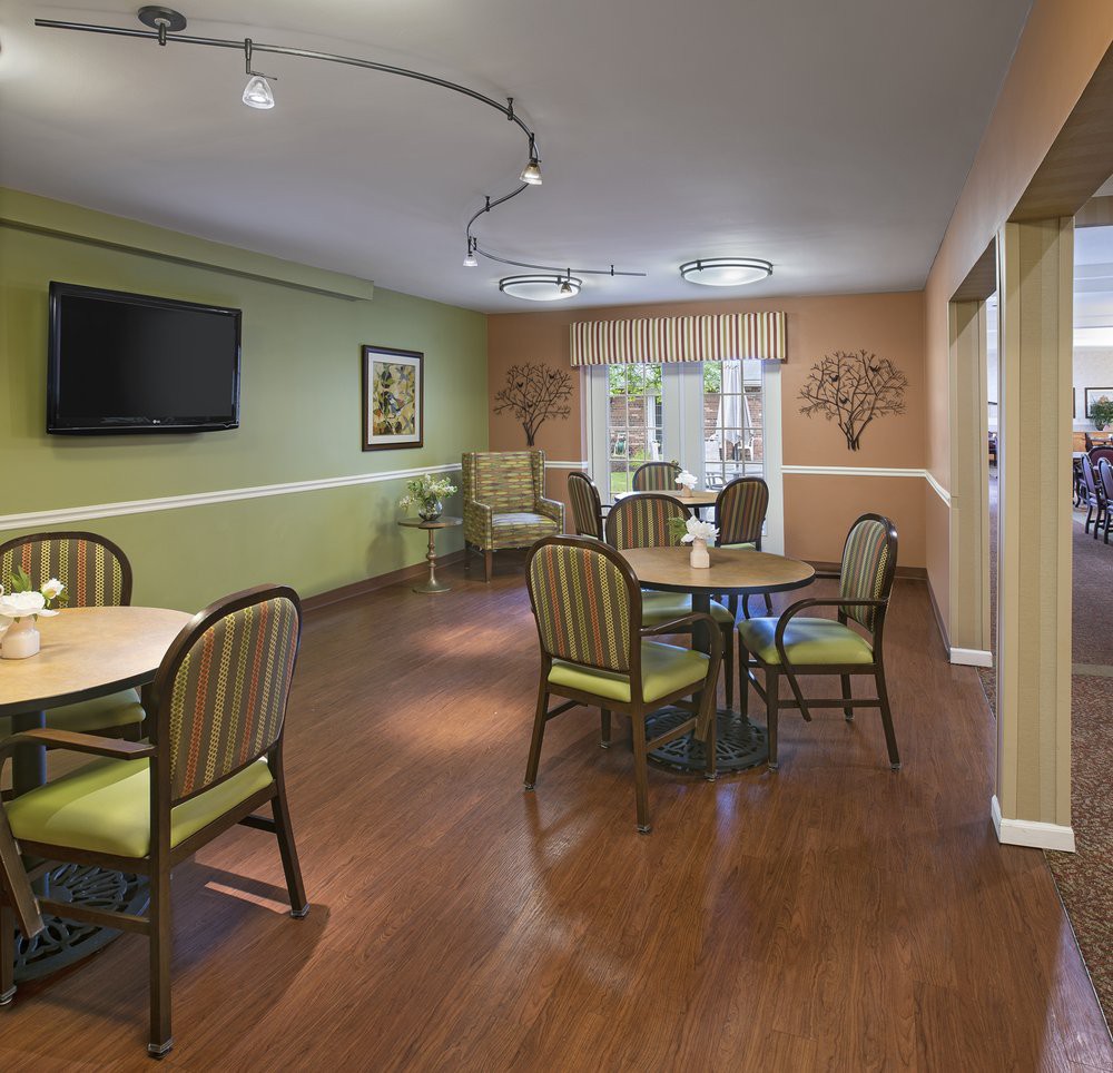 A cozy dining room with tables, chairs, and a television mounted on the green wall.