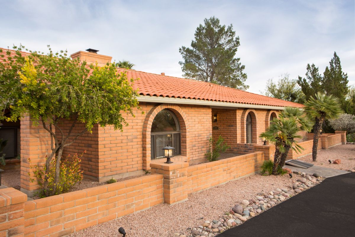 A brick house with arched windows and desert landscaping.